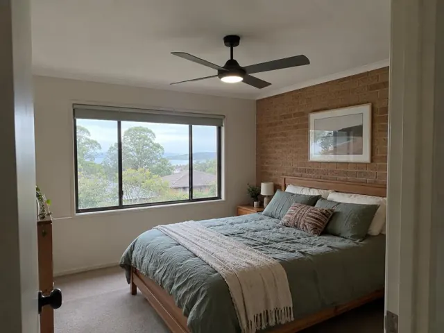 Bedroom with a ceiling fan, bed and brick feature wall in Avoca Beach