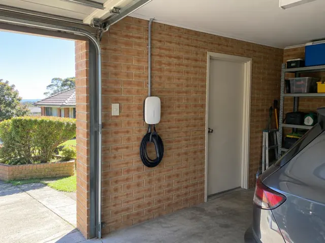 Wall-mounted EV charger with coiled cable on a brick garage wall beside a driveway in Green Point